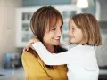 Uśmiechnięta mama i córka przytulają się, emanując ciepłem i bliskością. To kwintesencja rodzicielstwa bliskości.