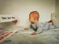 10 tygodniowe dziecko leży na brzuchu, patrząc na napis "Tata jest silny".