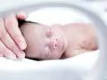 Delikatna dłoń otula głowę śpiącego wcześniaka.