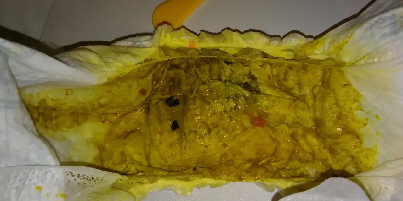 Żółta, luźna kupka w pieluszce, z widocznymi grudkami i kilkoma czerwonymi kropkami.